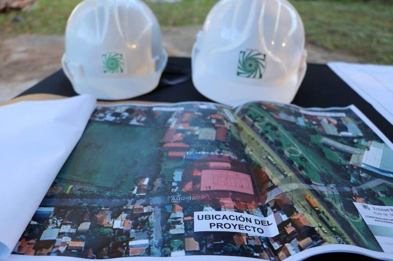 Dos cascos de seguridad blancos sobre un plano aéreo del área 'Aquidabán', que indica la ubicación del proyecto de construcción.