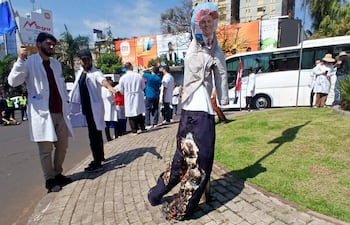 Grupo de médicos con batas blancas en protesta, incluyendo un hombre sosteniendo una bandera paraguaya y un muñeco de papel.