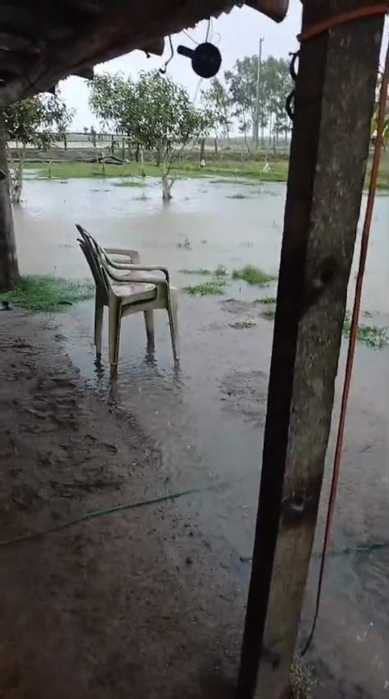 Silla plástica clara en terreno inundado con árboles de fondo, reflejando el impacto de las fuertes lluvias en la zona rural.