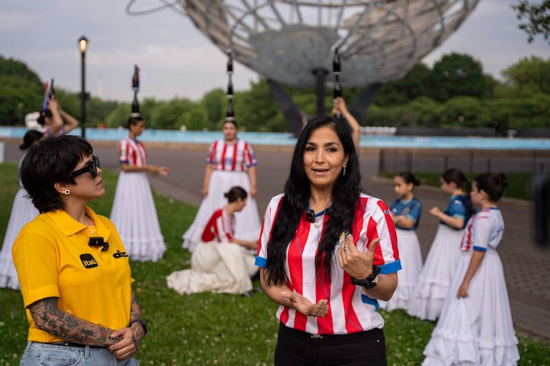 Lourdes Frutos con camiseta roja y blanca conversando en evento cultural, rodeada de mujeres en faldas largas y blusas coloridas.