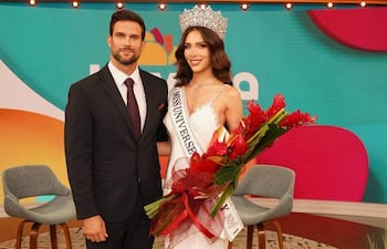 Gretha Matiauda con corona y vestido blanco sonríe sosteniendo un ramo, junto a un hombre en traje oscuro en un ambiente colorido.