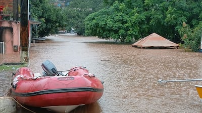 Embarcación inflable roja en agua marrón, rodeada de objetos flotantes y áreas habitacionales parcialmente sumergidas.
