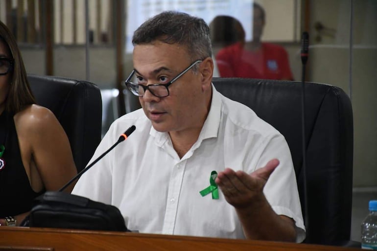 Humberto Blasco con camisa blanca y gafas habla hacia un micrófono, Rafael Ávila escucha desde su asiento a la izquierda.