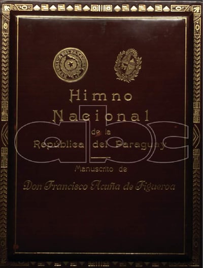 Manuscrito del Himno Nacional enmarcado, con escudos en los bordes y título en dorado.