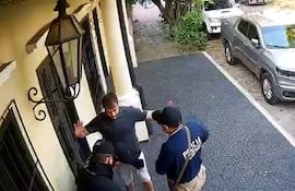 Tres hombres en ropa oscura; uno con camiseta azul de 'Policía' habla a otro que levanta las manos.