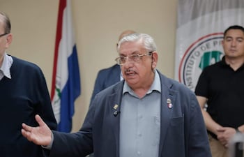 Isaías Fretes gesticula enfáticamente en camisa gris y saco oscuro, rodeado de personas escuchando atentos en un ambiente formal.