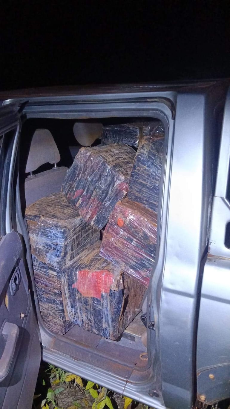 Asientos traseros de un vehículo con bultos envueltos en plástico, en un entorno rural y oscuro.