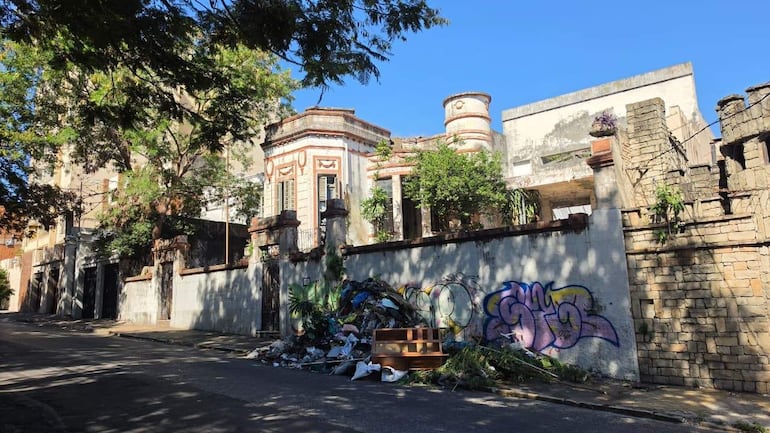 Fachada de la Casa de Serafina Dávalos con grafitis, basura y un sofá abandonado en un día soleado.