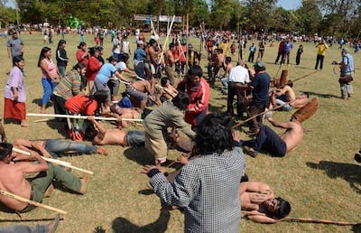 Grupo de hombres y mujeres, algunos semidesnudos, compitiendo con palos en un ambiente natural rodeado de espectadores.