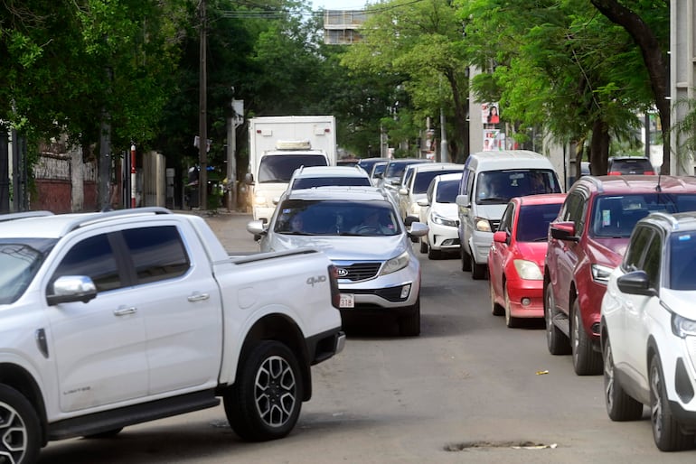 Camioneta blanca y automóvil gris en una calle congestionada rodeada de árboles y edificios.