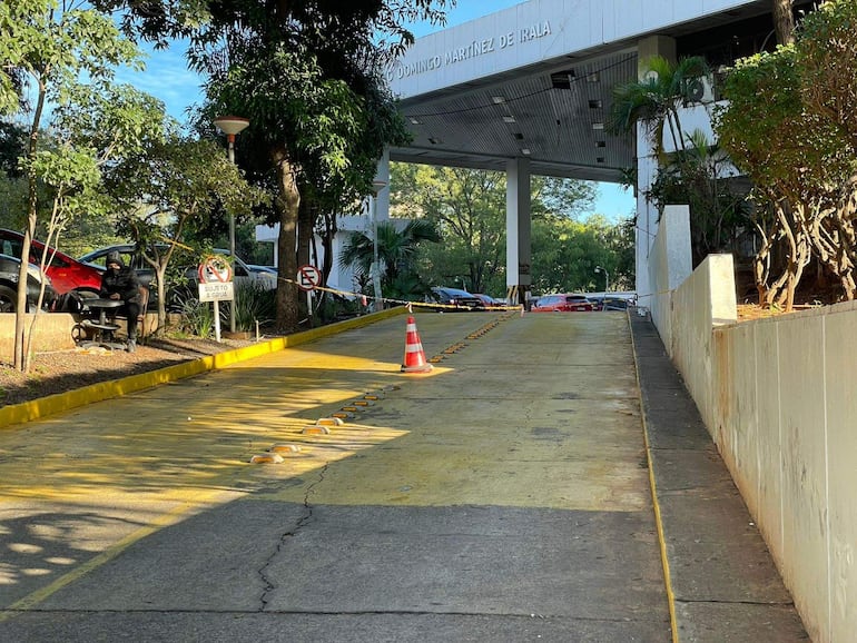 Hombre sentado en banco, vestido de negro, junto a vehículos y señal de 'Sujeto a grúa' en un entorno urbano.