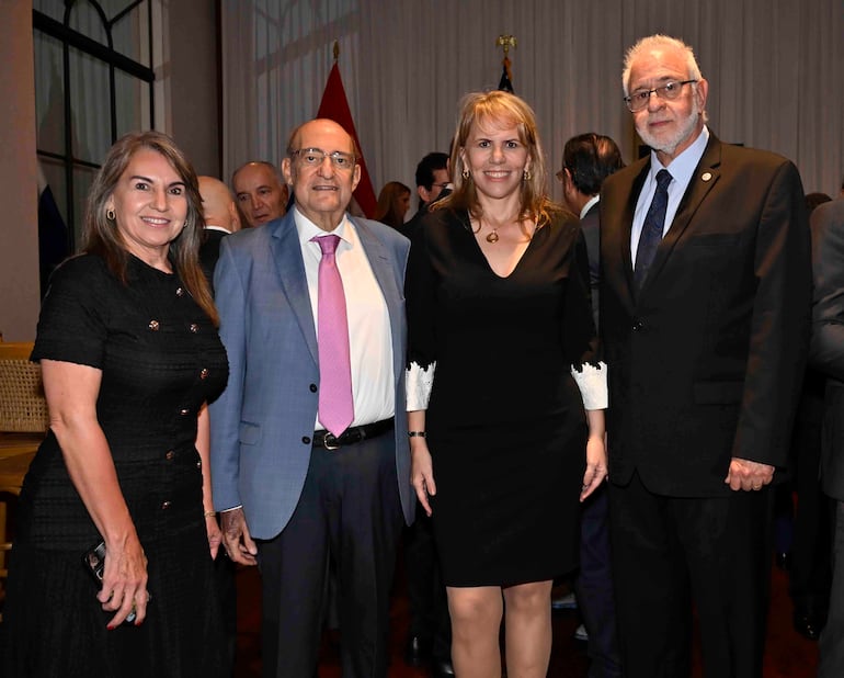 Liz Cramer en vestido negro, junto a hombre calvo en traje claro, otra mujer con cabello recogido y hombre mayor con barba canosa en evento formal.