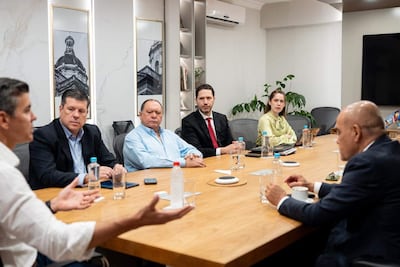 Santiago Peña en traje oscuro escucha a un orador. A su lado, Roberto Moreno y Javier Giménez, atentos y gesticulando en mesa moderna.