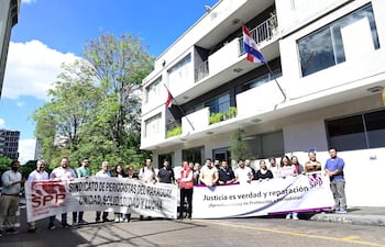 Grupo de personas sosteniendo pancartas en homenaje a Pablo Medina frente a una sede del SPP, con cielo azul de fondo.