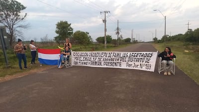 Seis personas en la manifestación, una mujer con top de animal print y otra con camiseta blanca sosteniendo la bandera paraguaya.