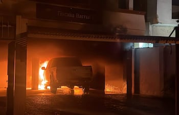 Un vehículo blanco ardiendo en llamas en un garaje, con humo visible en un ambiente nocturno.