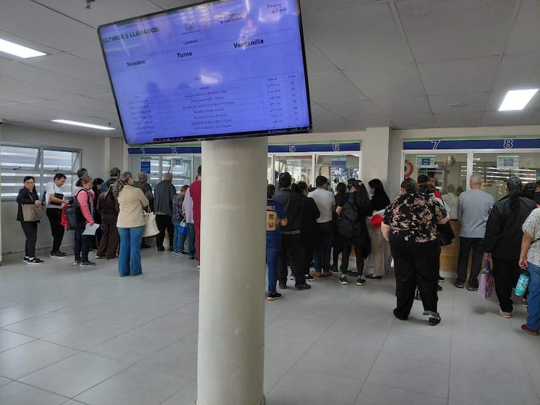 Grupo diverso de personas en fila, concentrados en el proceso de espera en una oficina del IPS.