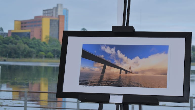 Fotografía enmarcada de un puente sobre el agua, presentada en una galería iluminada, sin personas visibles.