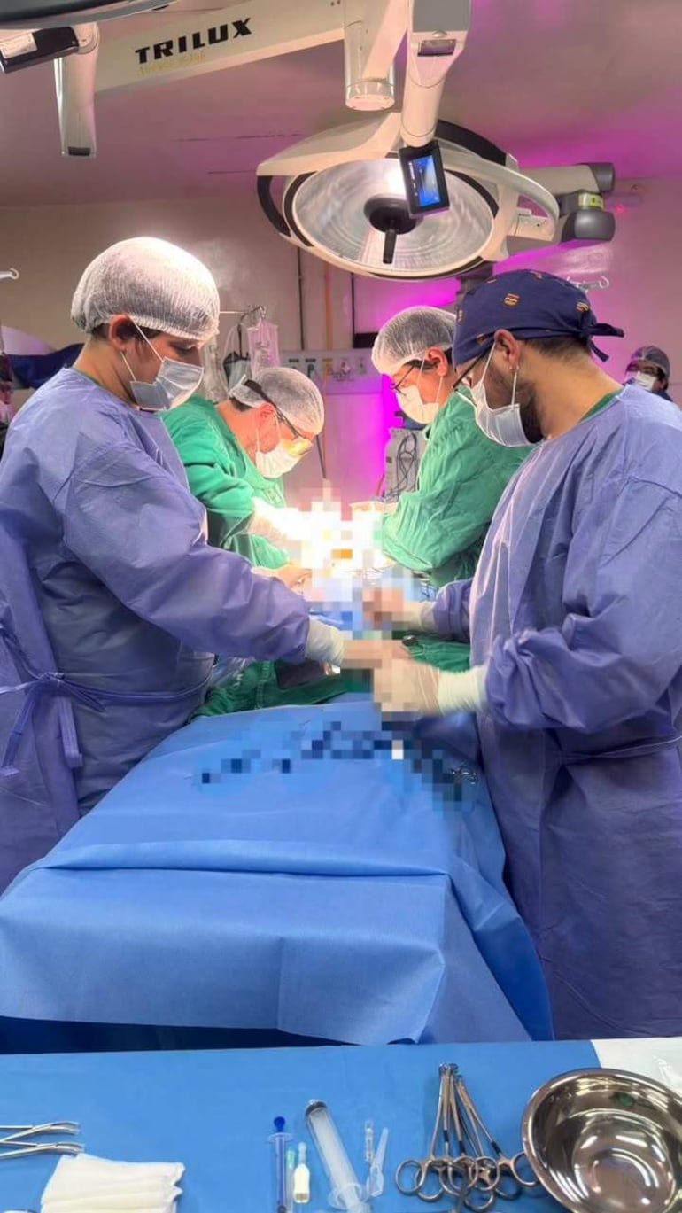 Grupo de seis médicos en quirófano, vestidos con batas y mascarillas, trabajando en la operación de una paciente.