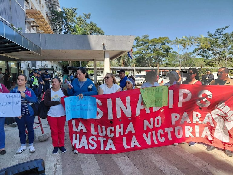 Grupo de manifestantes en camiseta de colores, sosteniendo pancarta roja con mensaje de lucha y expresión de protesta.