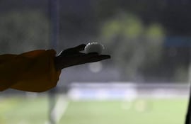 Una mano sostiene un objeto esférico blanco en un espacio oscuro, con una prenda amarilla visible en el brazo.