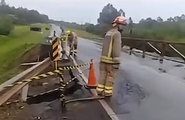 Cuatro trabajadores en trajes de protección y cascos reparan un bache en una carretera rodeada de vegetación.