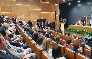 Emiliano Rolón Fernández detrás de un podio, rodeado de hombres en traje en un ambiente formal con plantas decorativas.