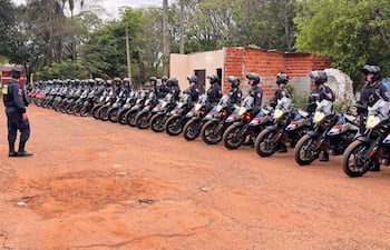Formación de uniformados en motocicletas negras, rodeados de vegetación, mientras un oficial permanece de pie en atención.