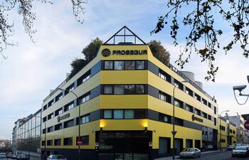 Edificio moderno de Prosegur en colores amarillos y negros, con vegetación en la azotea y coches estacionados.