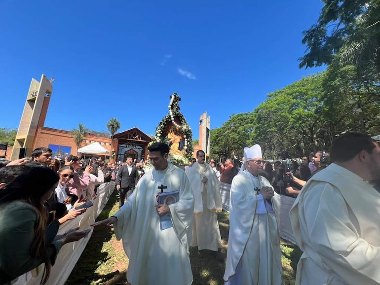Cuatro sacerdotes en túnicas blancas interactúan con una multitud de asistentes en un ambiente festivo y de recogimiento.