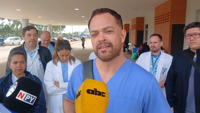 Grupo de seis médicos, uno con lab coat blanco y micrófono, expresan su postura sobre la situación laboral en el hospital.
