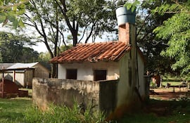 Estructura pequeña de paredes blancas y techo de tejas rojas en medio de vegetación densa, sin personas visibles.