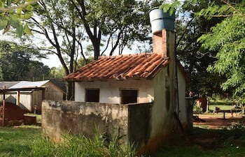 Estructura pequeña de paredes blancas y techo de tejas rojas en medio de vegetación densa, sin personas visibles.
