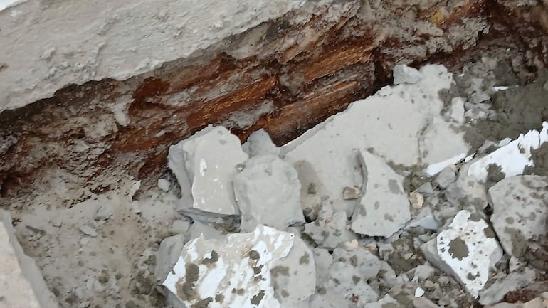 Sección de piso en reparación con escombros de concreto y yeso, afectada por humedad en área interior.