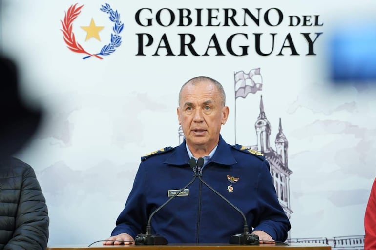 Julio Rubén Fullaondo en uniforme hablando frente a un micrófono, con fondo del Gobierno del Paraguay, mientras escucha otra persona a su lado.
