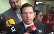 Alejandro Aguilera en traje oscuro, dirigiéndose a un grupo de periodistas en conferencia de prensa, con expresión seria.