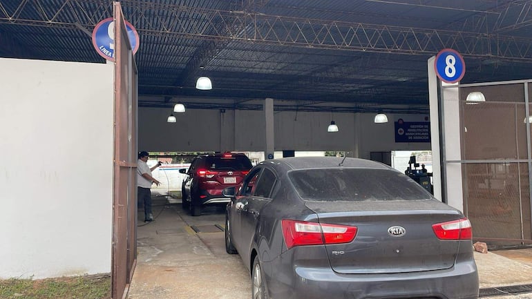 Hombre en camisa blanca y pantalones oscuros dirige el tráfico entre un coche gris y uno rojo en un control vehicular.