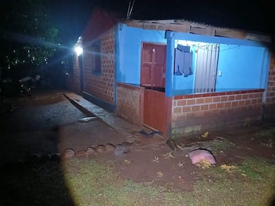 Casa de ladrillos azules con puerta de madera y ventana metálica, sin personas visibles en el entorno rural y tranquilo.