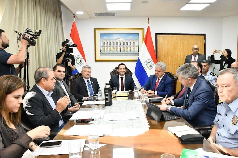 Raúl Latorre en el centro con expresión seria, rodeado de hombres en traje, Johanna Ortega a la izquierda, banderas de Paraguay decorando el fondo.