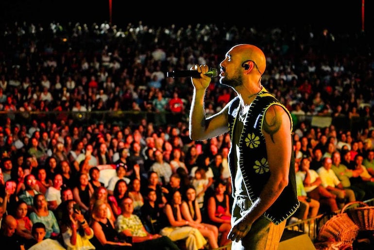 Abel Pintos en el escenario, con chaleco decorado, cantando frente a una multitud entusiasta que aplaude y graba con sus móviles.
