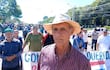 Hombre mayor con sombrero habla en manifestación, mientras una mujer de blusa colorida sostiene un cartel en un ambiente cívico.
