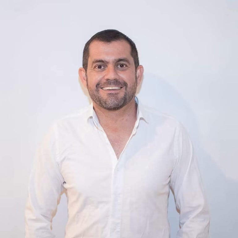 Sergio Ramirez vestido con camisa blanca, sonriente, posando en un fondo blanco.