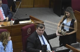 La senadora Noelia Cabrera y el Dionisio Amarilla conversan, mientras Amarilla toma dos piñas de una funcionaria del Congreso.