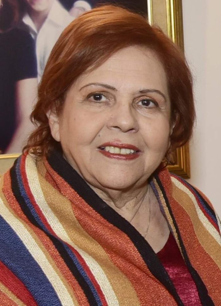 Mujer de cabello castaño claro y corto, vestida con abrigo rojo, naranja, amarillo y negro, sonriendo hacia la cámara.