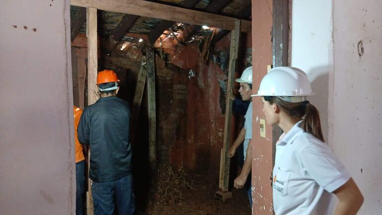 Cuatro personas con cascos, dos de blanco y uno naranja, realizan tareas de reconstrucción en un ambiente deteriorado.