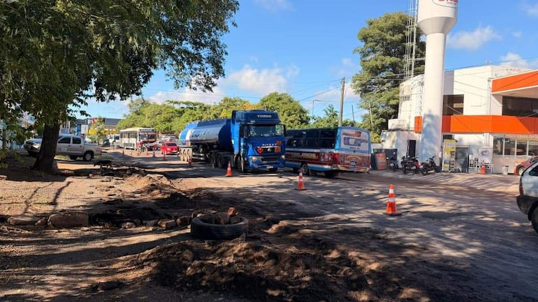 Escena urbana con camiones y autobús en movimiento, señalización de trabajo en la vía y árboles en el entorno.