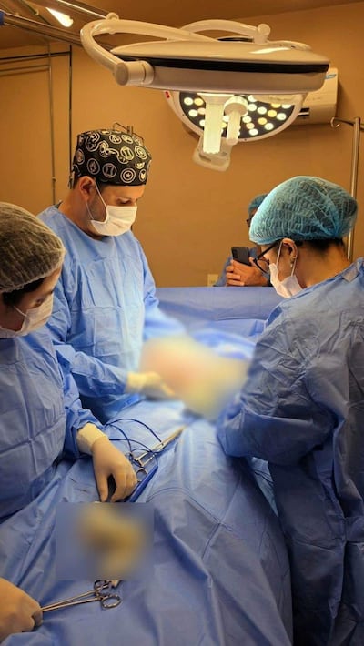 Cuatro personas en un quirófano iluminado, dos cirujanos concentrados en la operación, mientras otros observan con vestimenta estéril.