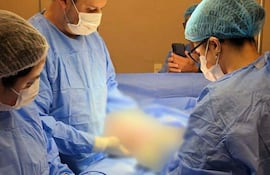 Cuatro personas en un quirófano iluminado, dos cirujanos concentrados en la operación, mientras otros observan con vestimenta estéril.