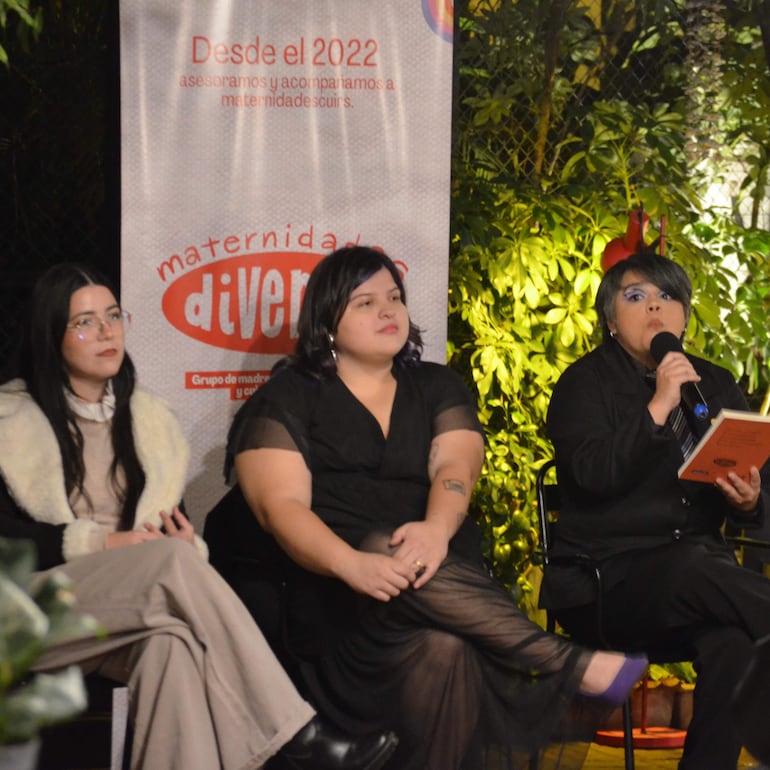 Lía Benítez Flecha, con cabello corto y plateado, presenta su libro mientras dos mujeres la escuchan atentamente en un entorno al aire libre.