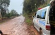Ambulancia blanca con símbolo de emergencias atascada en barro, mientras un hombre sostiene un palo evaluando la situación.